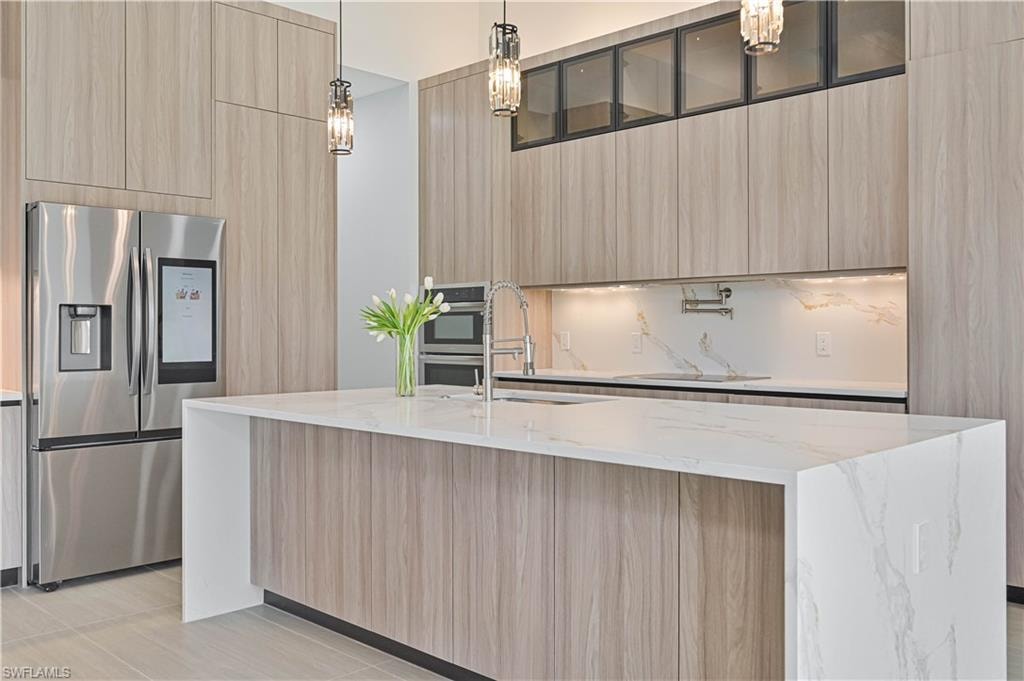 Kitchen with decorative light fixtures, light stone countertops, light wood finish cabinets, stainless steel appliances, and modern cabinets