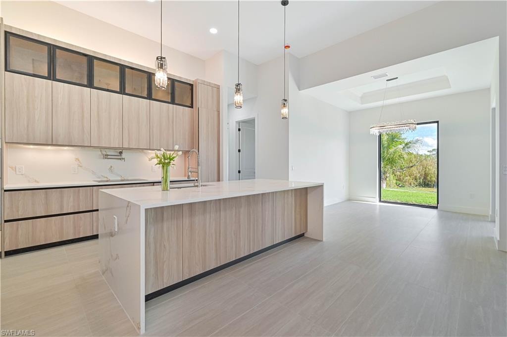 Kitchen with light wood finish cabinetry, pendant lighting, light stone counters, and a tray ceiling