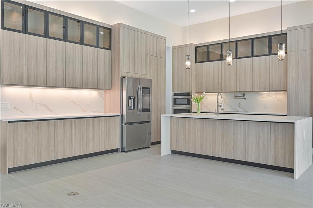 Kitchen with stainless steel appliances, modern cabinets, light stone counters, a kitchen island with sink, and light wood finish cabinets
