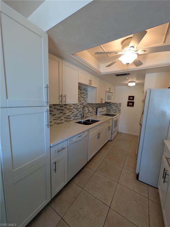 Kitchen with white cabinetry, white appliances, decorative backsplash, a tray ceiling, and a ceiling fan