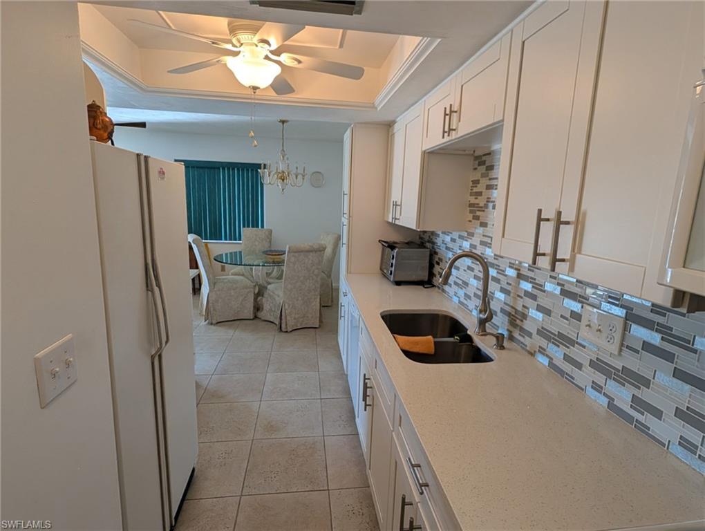 Kitchen with tasteful backsplash, a tray ceiling, freestanding refrigerator, light stone countertops, and white cabinets