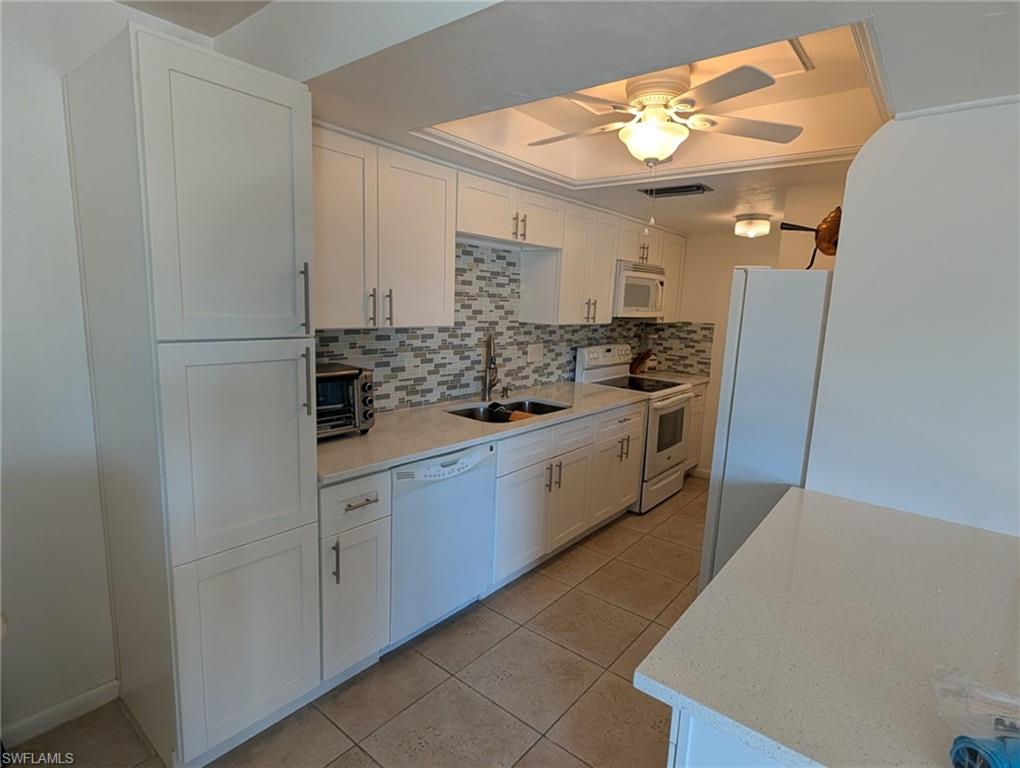 Kitchen with white cabinetry, white appliances, tasteful backsplash, and light stone countertops