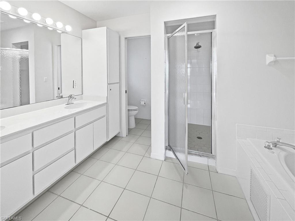Master Bathroom with double vanity, a shower stall, light tile patterned flooring, and a garden tub