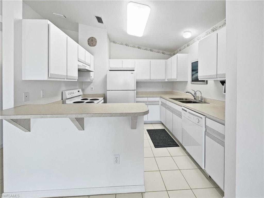 Kitchen featuring a kitchen bar, white cabinets, white appliances, lofted ceiling, and light countertops
