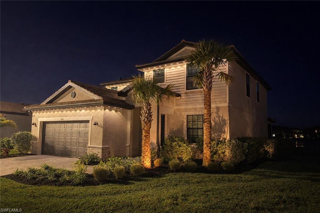 View of front facade with a yard, a garage, driveway, stucco siding, and stone siding