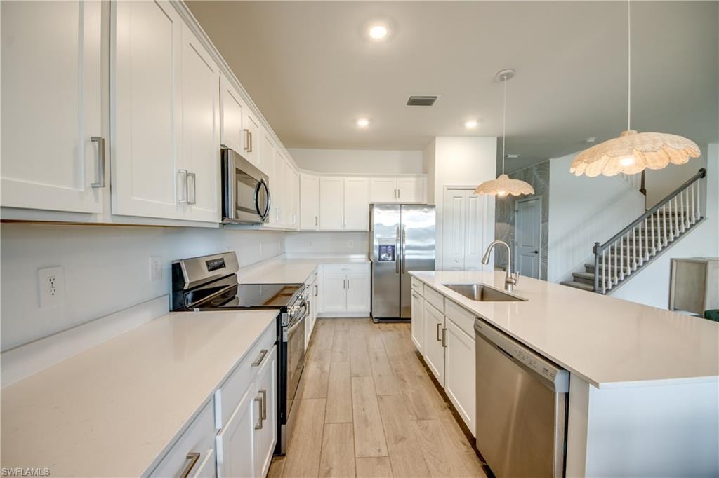 Kitchen with appliances with stainless steel finishes, pendant lighting, a center island with sink, white cabinetry, and light wood-type flooring