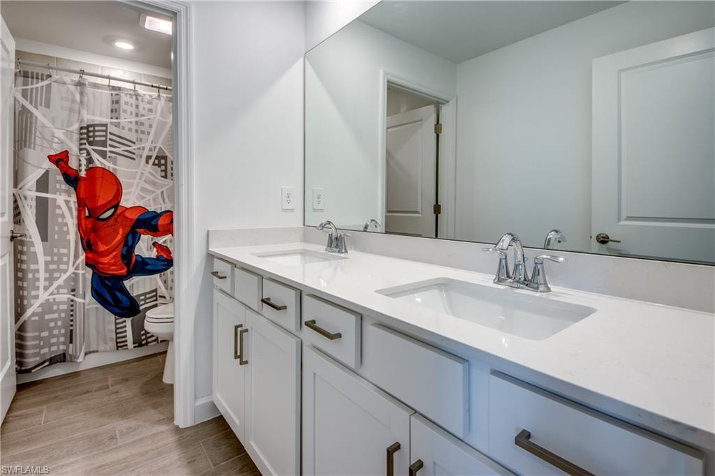 Full bathroom with double vanity, curtained shower, and wood tiled floors