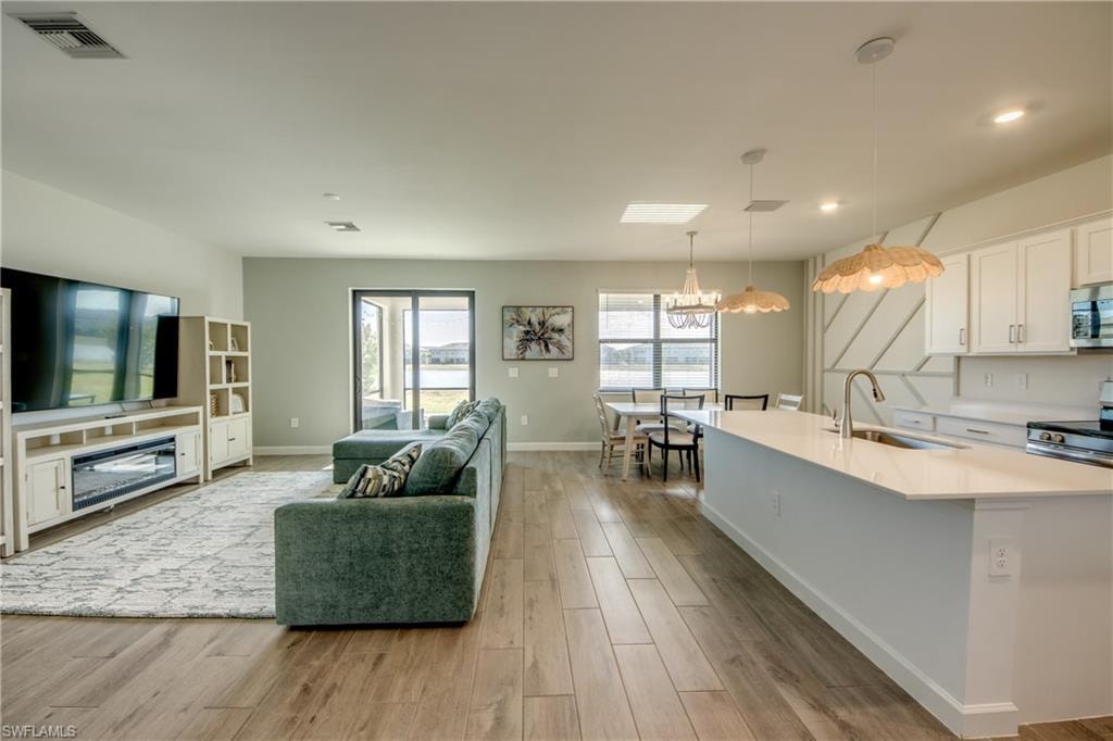 Kitchen featuring white cabinetry, light wood finished floors, pendant lighting, an island with sink, and stainless steel microwave