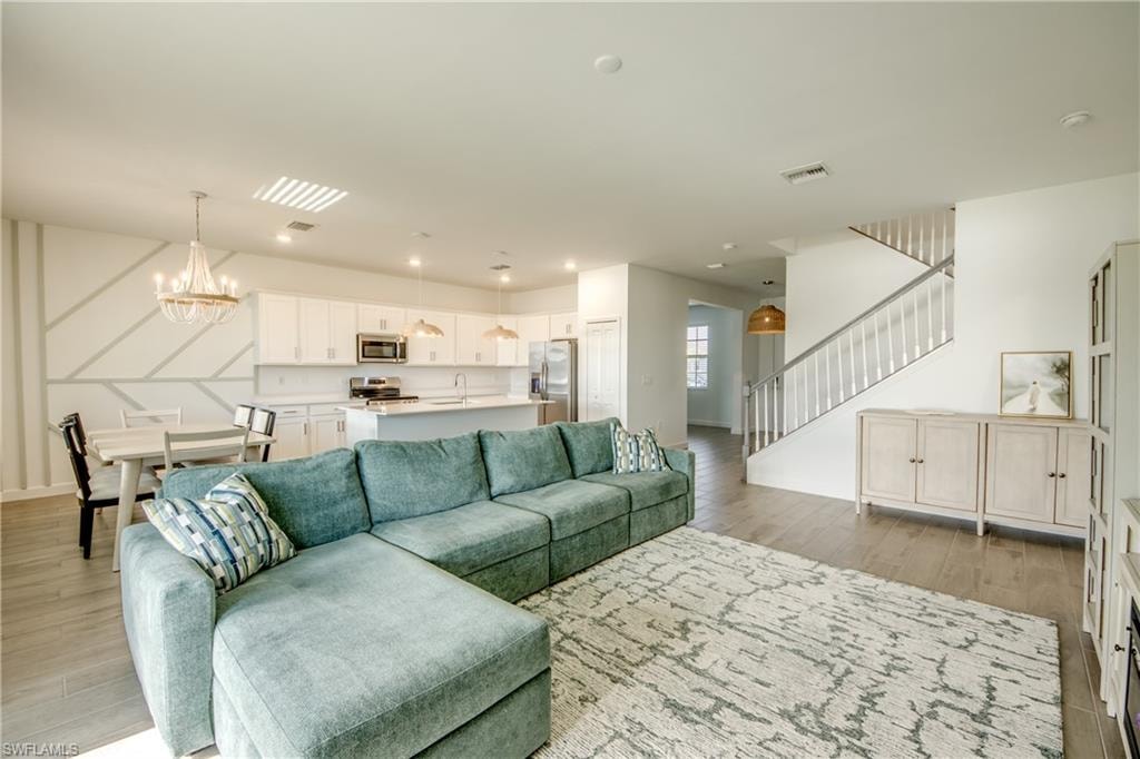 Living area featuring light wood-style flooring, stairs, and a chandelier