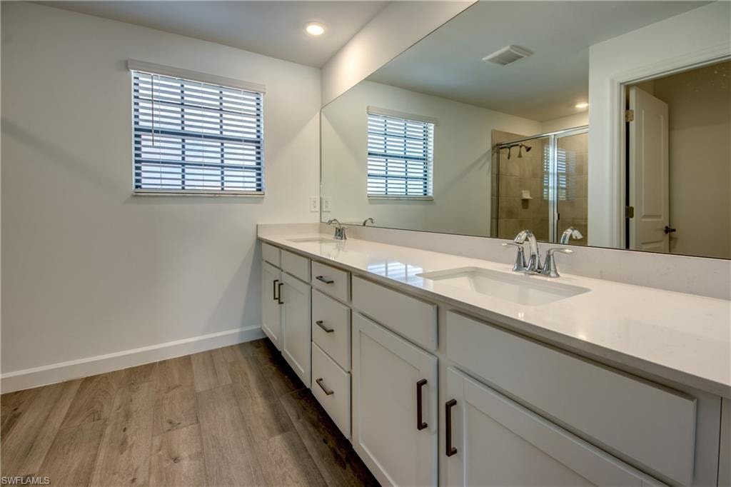 Bathroom featuring double vanity, a shower stall, and light wood-style floors