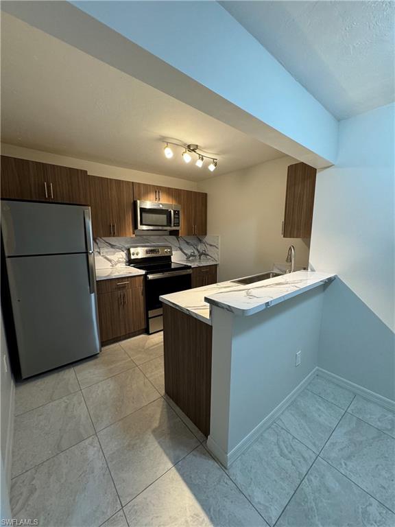 Kitchen featuring appliances with stainless steel finishes, a peninsula, modern cabinets, and light stone counters