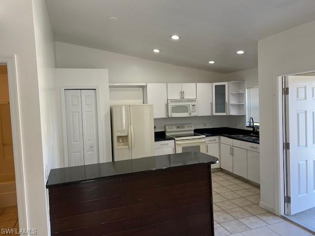 Kitchen with open shelves, vaulted ceiling, white appliances, white cabinets, and dark countertops