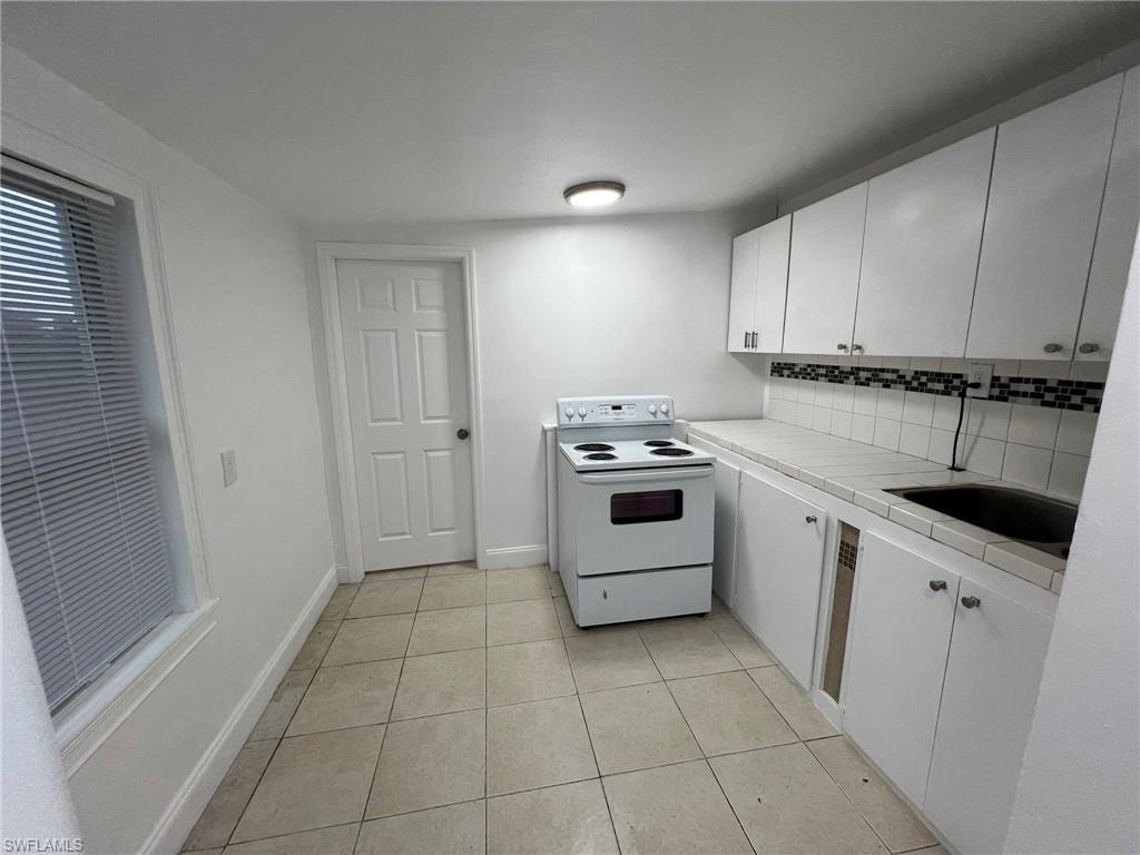 Kitchen featuring tile countertops, white cabinetry, white electric range oven, decorative backsplash, and light tile patterned floors
