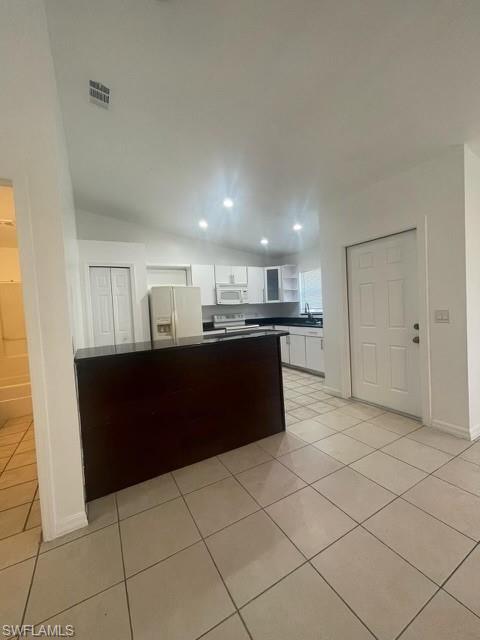 Kitchen with white cabinets, dark countertops, white appliances, light tile patterned floors, and recessed lighting