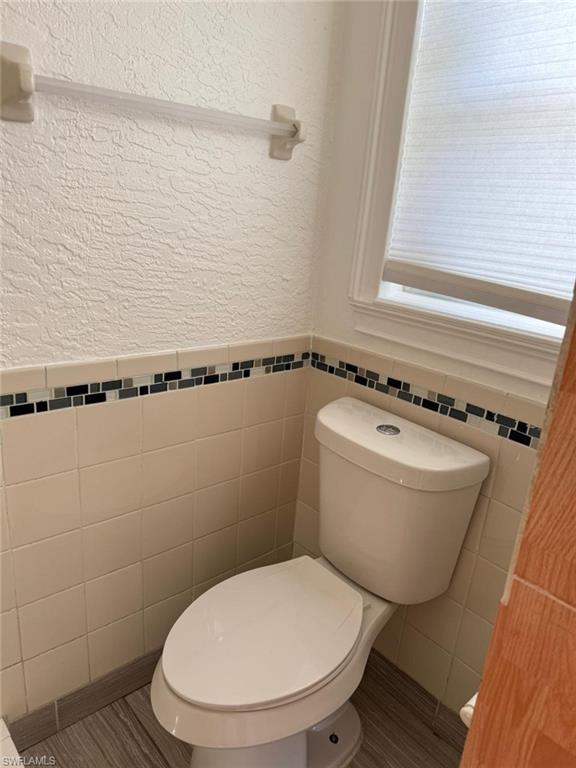 Bathroom featuring a textured wall, wainscoting, and tile walls
