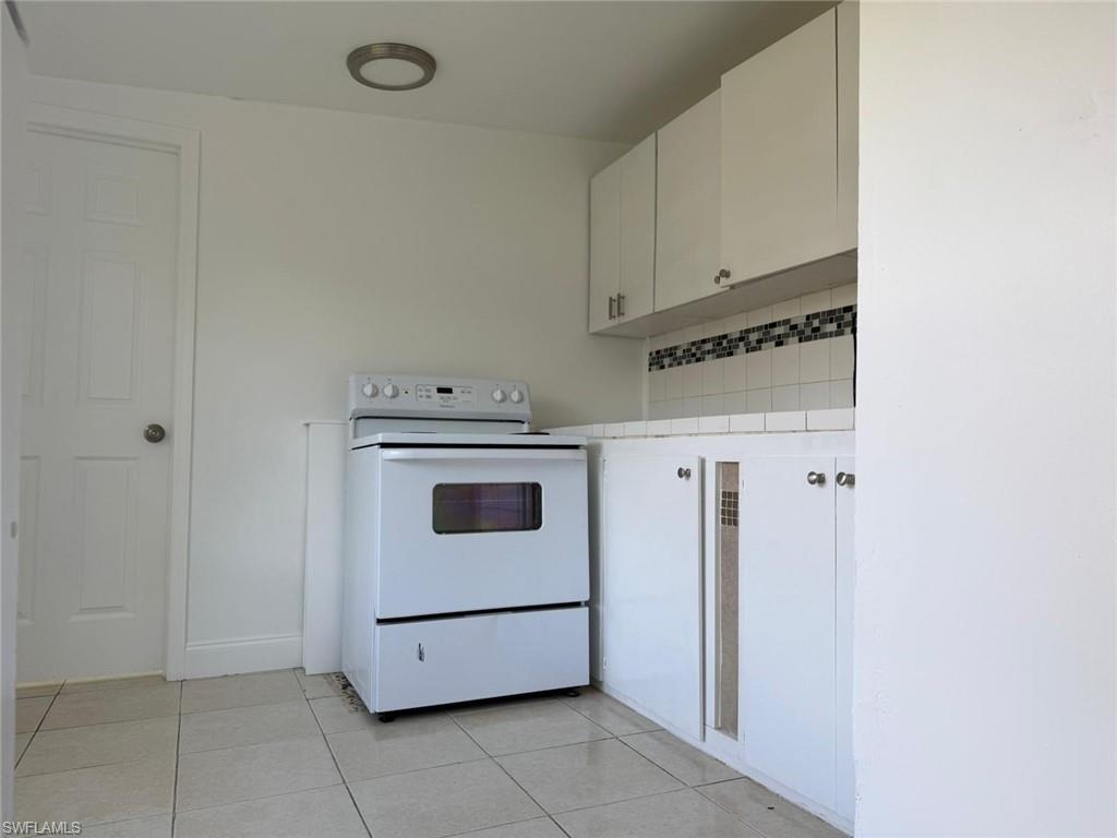 Kitchen with white cabinets, white electric range, light tile patterned floors, and tasteful backsplash