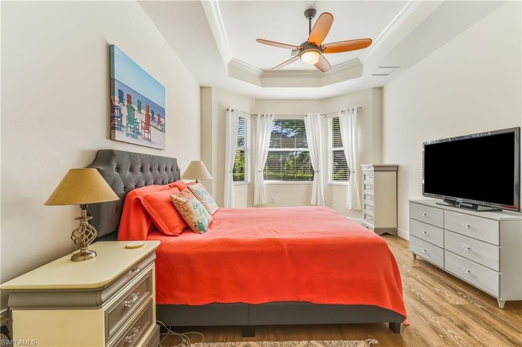 Bedroom with crown molding, light wood-style flooring, ceiling fan, and a raised ceiling