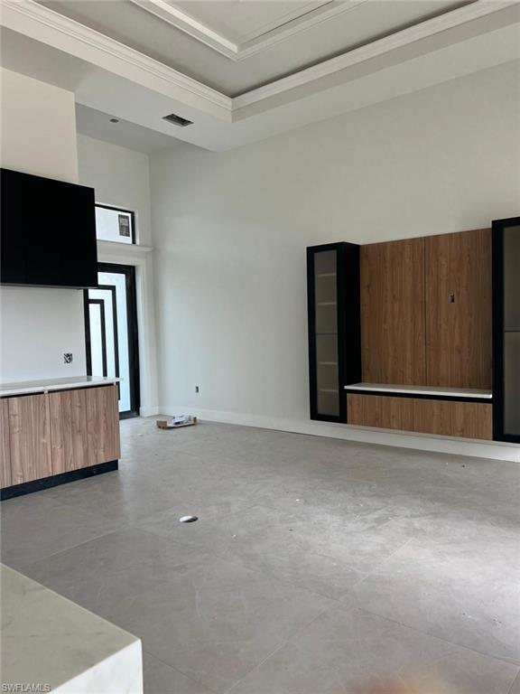 Unfurnished living room featuring ornamental molding, a towering ceiling, concrete flooring, and a tray ceiling