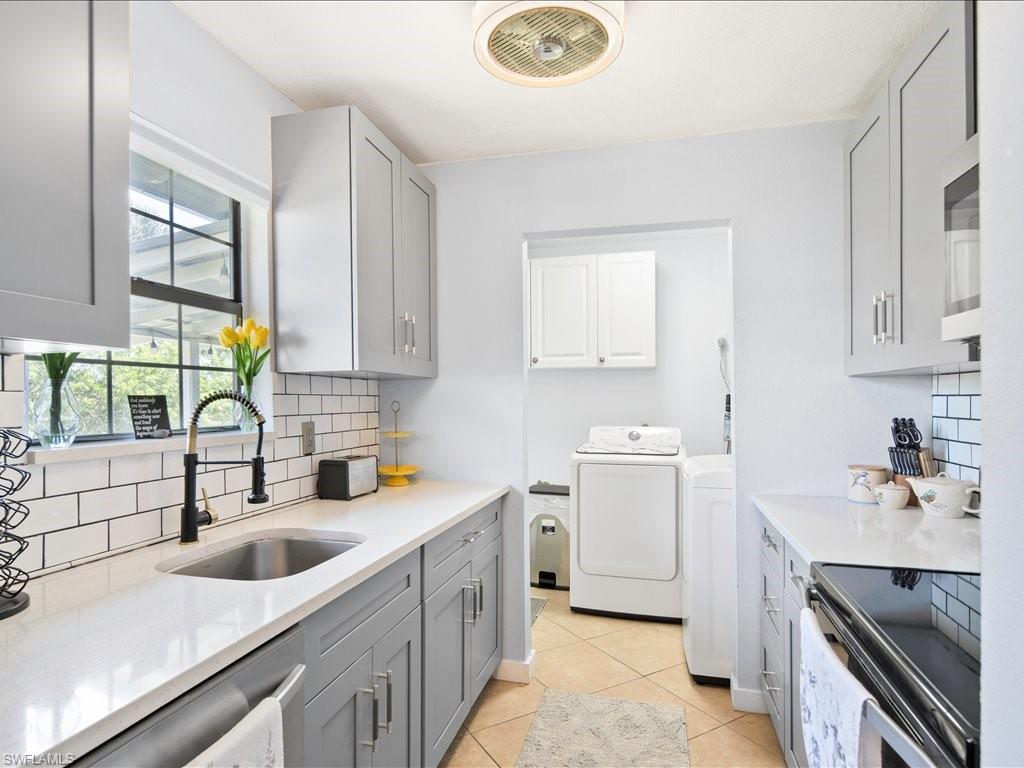 Kitchen with gray cabinets, appliances with stainless steel finishes, tasteful backsplash, light stone countertops, and washer and dryer