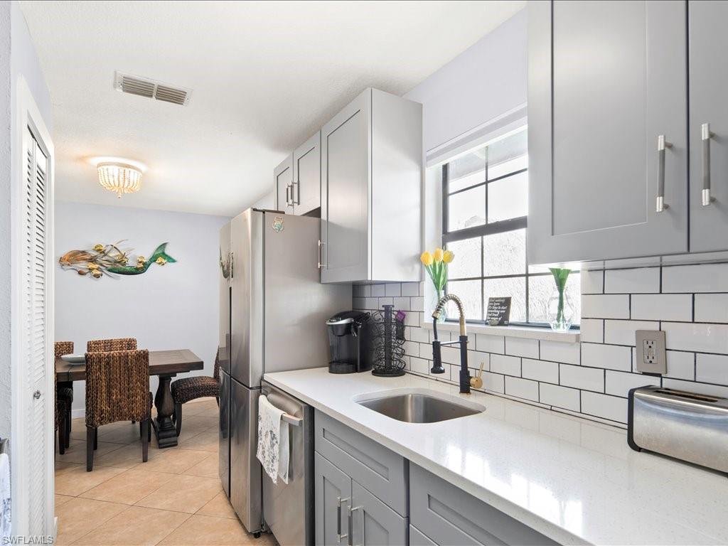Kitchen featuring gray cabinets, light tile patterned flooring, light stone countertops, backsplash, and dishwasher