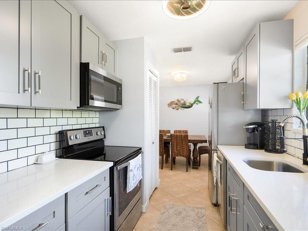 Kitchen featuring gray cabinetry, decorative backsplash, appliances with stainless steel finishes, light stone countertops, and light tile patterned flooring