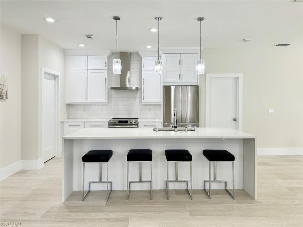 Kitchen with a breakfast bar area, light stone counters, stainless steel appliances, wall chimney range hood, and recessed lighting