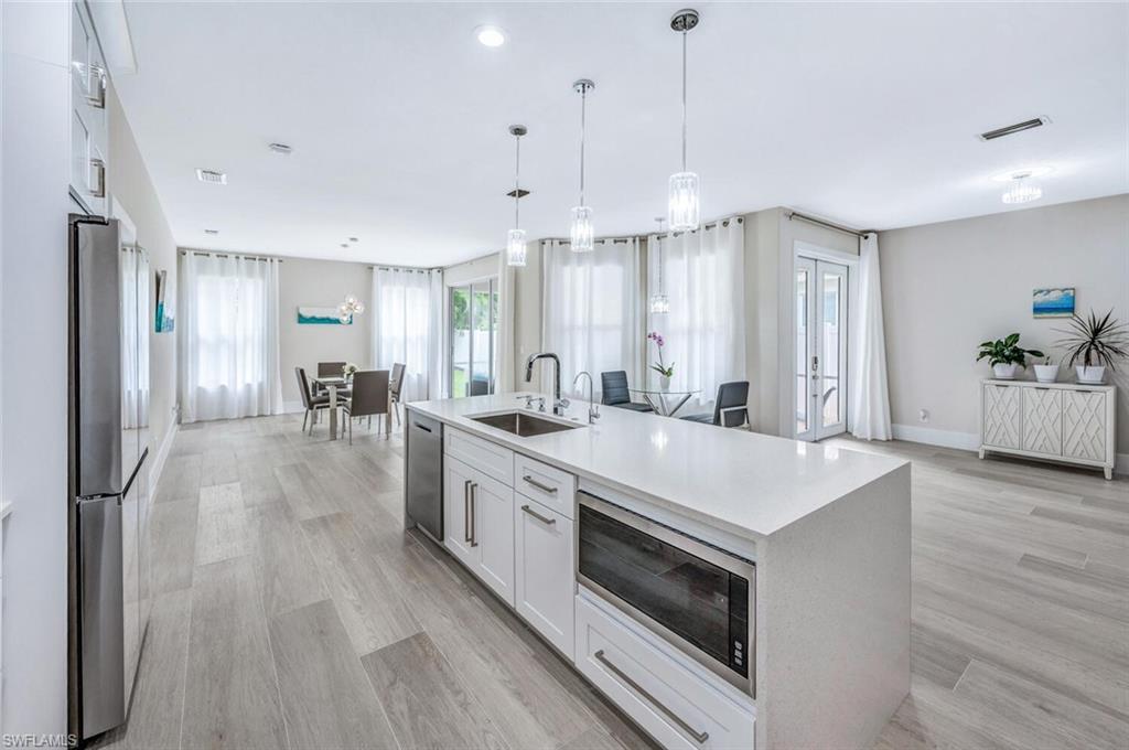 Kitchen featuring white cabinets, appliances with stainless steel finishes, light stone countertops, pendant lighting, and light wood-style floors