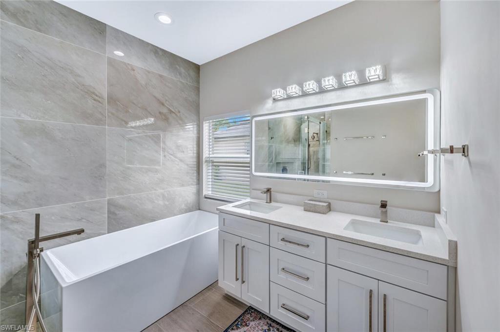Full bathroom with tile walls, a freestanding bath, double vanity, a shower stall, and recessed lighting