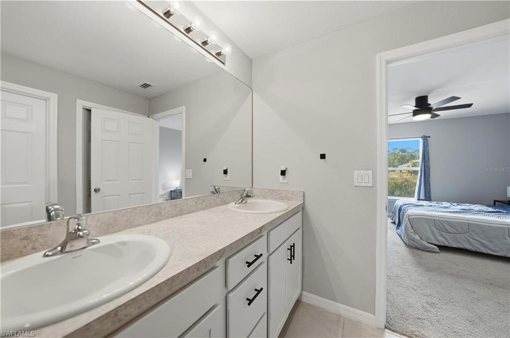 Ensuite bathroom with double vanity, light colored carpet, a ceiling fan, and light tile patterned floors