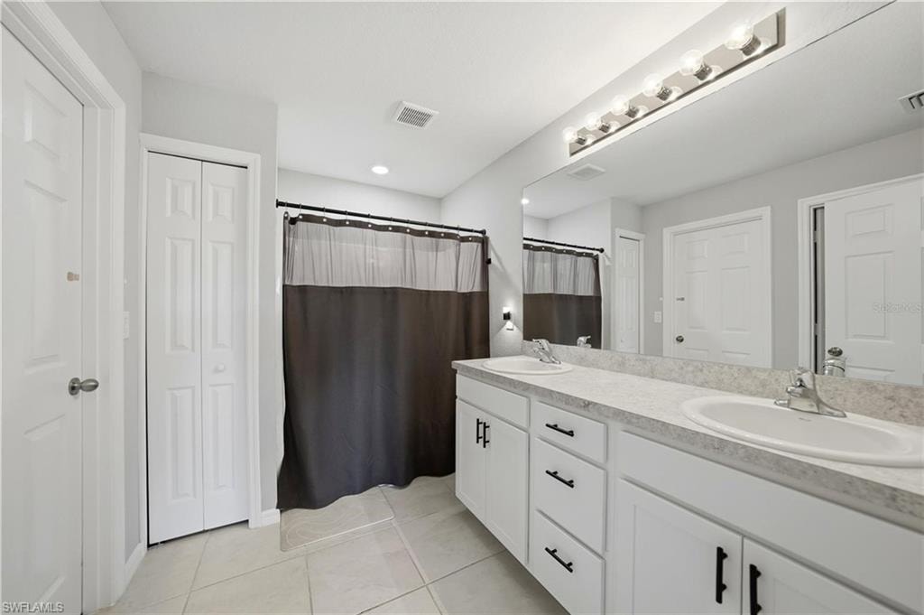 Full bathroom featuring a closet, double vanity, a shower with shower curtain, and light tile patterned floors