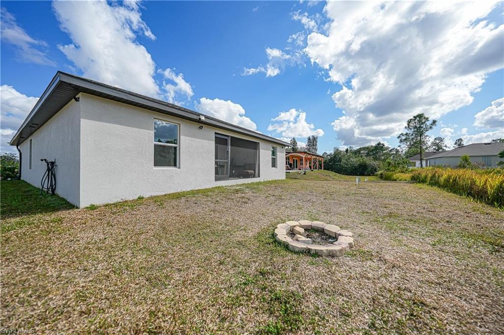 Rear view of property with stucco siding, a lawn, and an outdoor fire pit