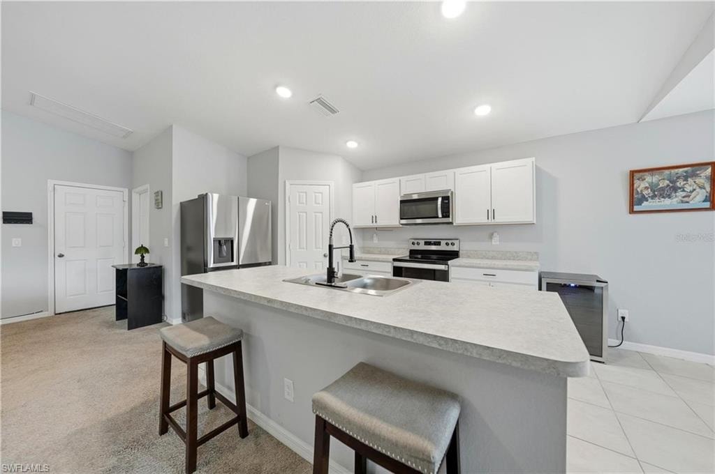 Kitchen featuring a breakfast bar area, light countertops, appliances with stainless steel finishes, white cabinetry, and a center island with sink