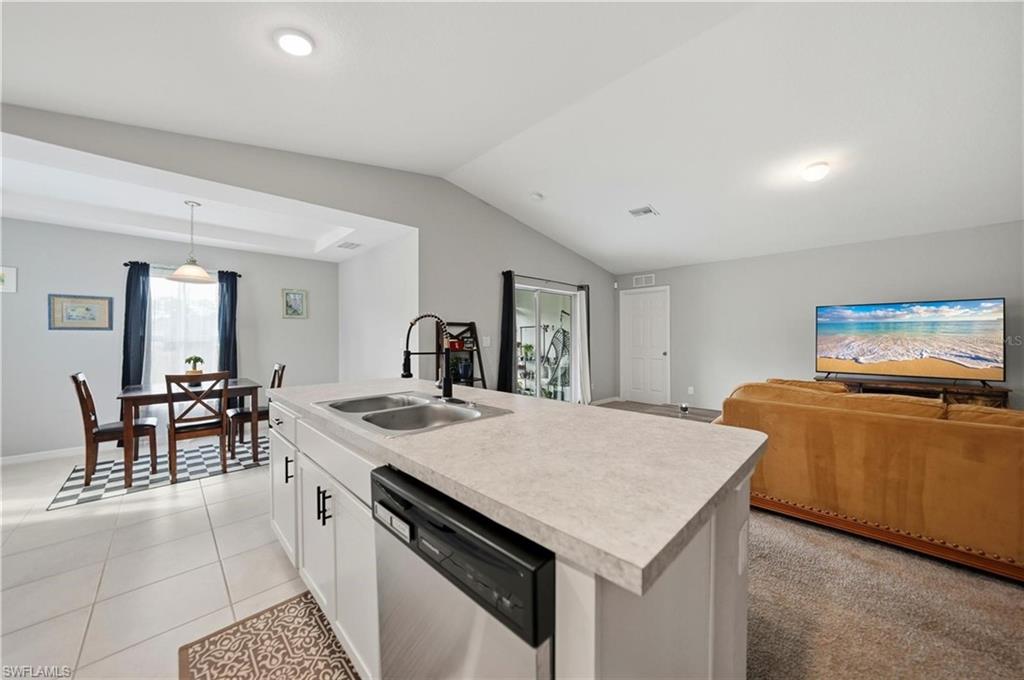 Kitchen featuring light countertops, dishwasher, white cabinetry, a center island with sink, and open floor plan