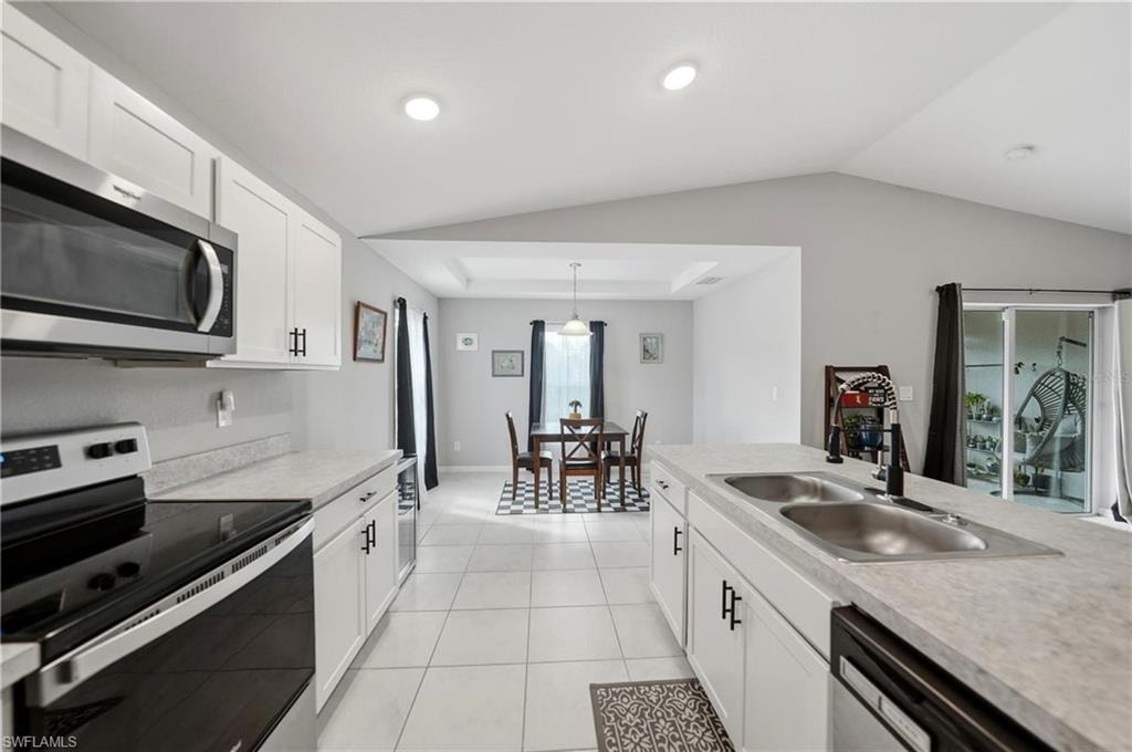 Kitchen with appliances with stainless steel finishes, white cabinets, light countertops, and vaulted ceiling
