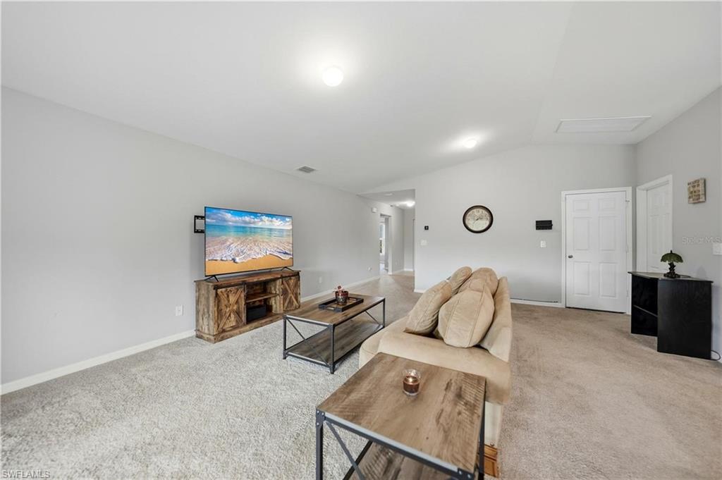 Living area featuring light colored carpet, lofted ceiling, and attic access