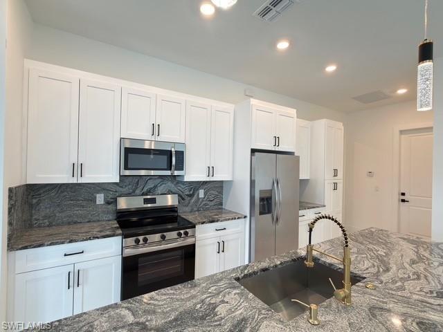 Kitchen featuring backsplash, dark stone counters, stainless steel appliances, white cabinetry, and decorative light fixtures
