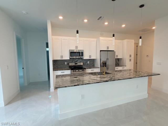 Kitchen featuring dark stone countertops, stainless steel appliances, backsplash, and white cabinetry