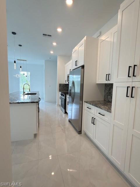 Kitchen featuring stainless steel appliances, white cabinets, tasteful backsplash, dark stone counters, and recessed lighting