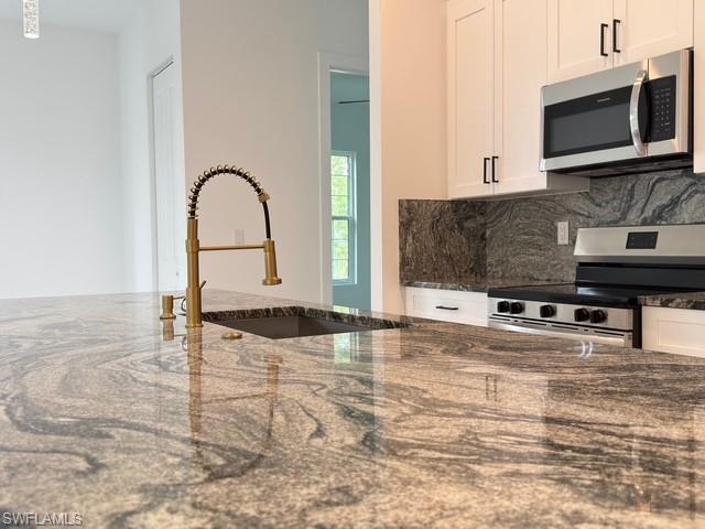 Kitchen featuring white cabinets, dark stone counters, pendant lighting, an island with sink, and open floor plan