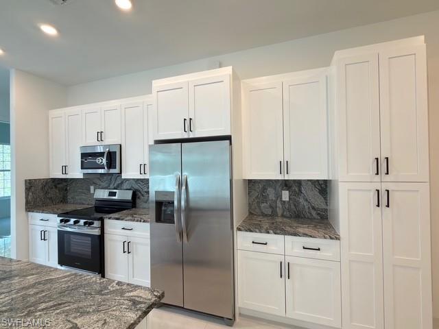 Kitchen with hanging light fixtures, stainless steel appliances, dark stone counters, white cabinetry, and decorative backsplash