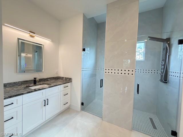 Full bath featuring two vanities, a shower stall, and light tile patterned flooring
