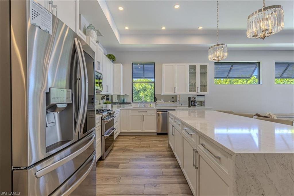 Kitchen featuring stainless steel appliances, glass insert cabinets, white cabinetry, recessed lighting, and light stone counters