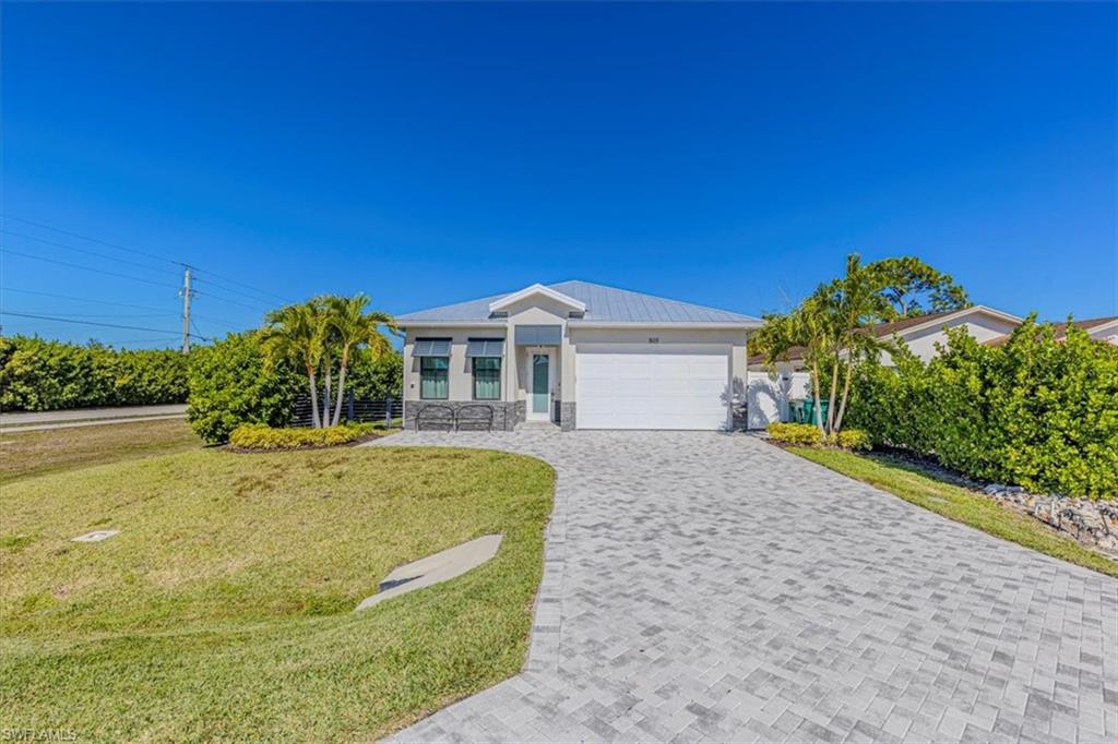 Single story home with a front lawn, decorative driveway, an attached garage, stone siding, and a metal roof