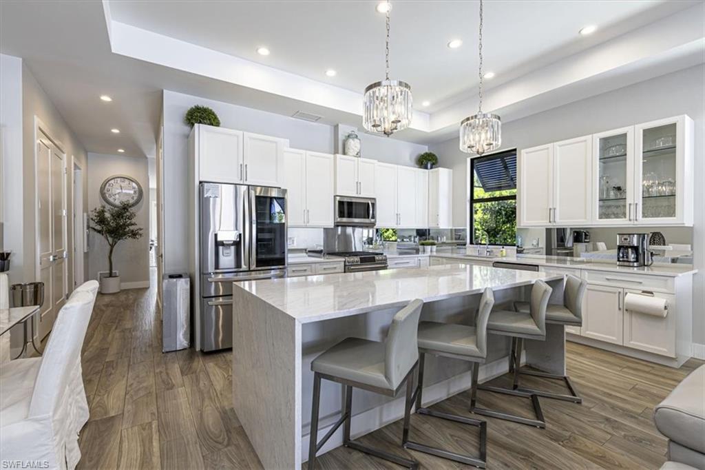 Kitchen with a raised ceiling, stainless steel appliances, decorative light fixtures, light stone counters, and white cabinets