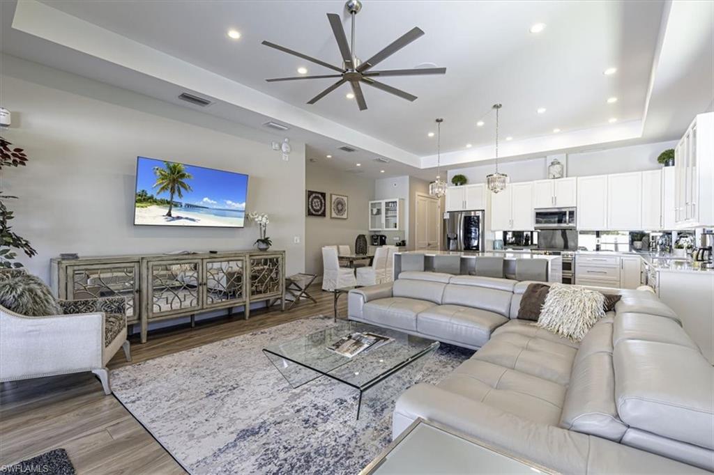 Living area with a tray ceiling, light wood-style flooring, a ceiling fan, and recessed lighting
