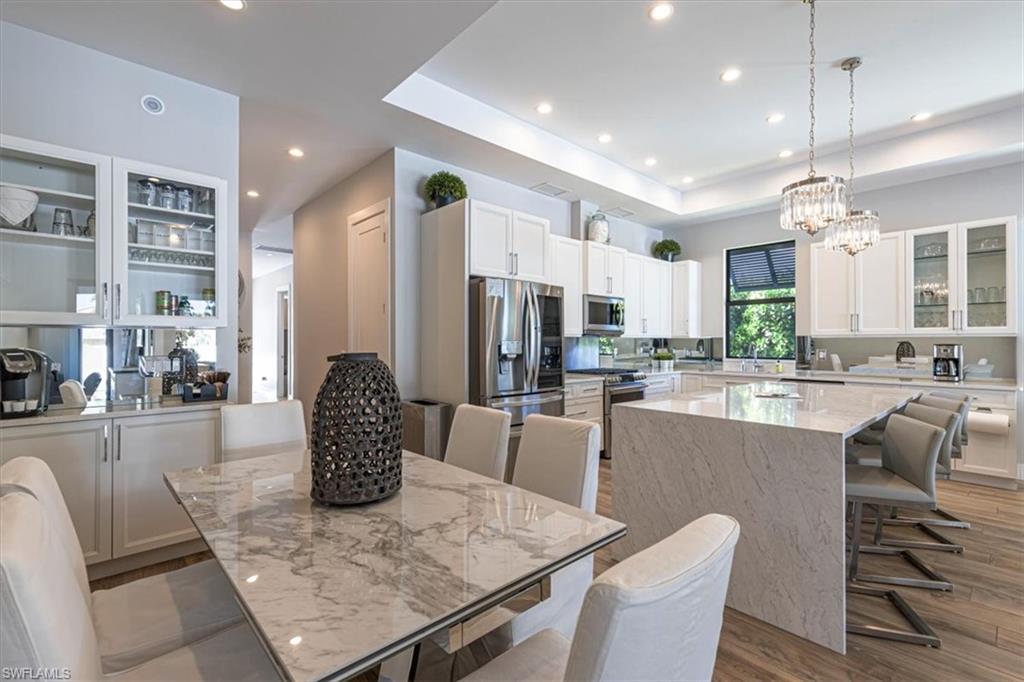 Kitchen featuring glass insert cabinets, a breakfast bar area, a center island, light stone counters, and white cabinetry