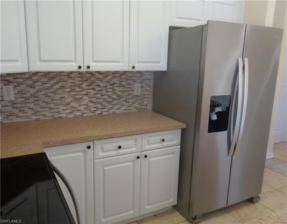 Kitchen featuring white cabinets, backsplash, stainless steel side by side door refrigerator with ice dispenser, backsplash, light tile patterned floors, and light countertops