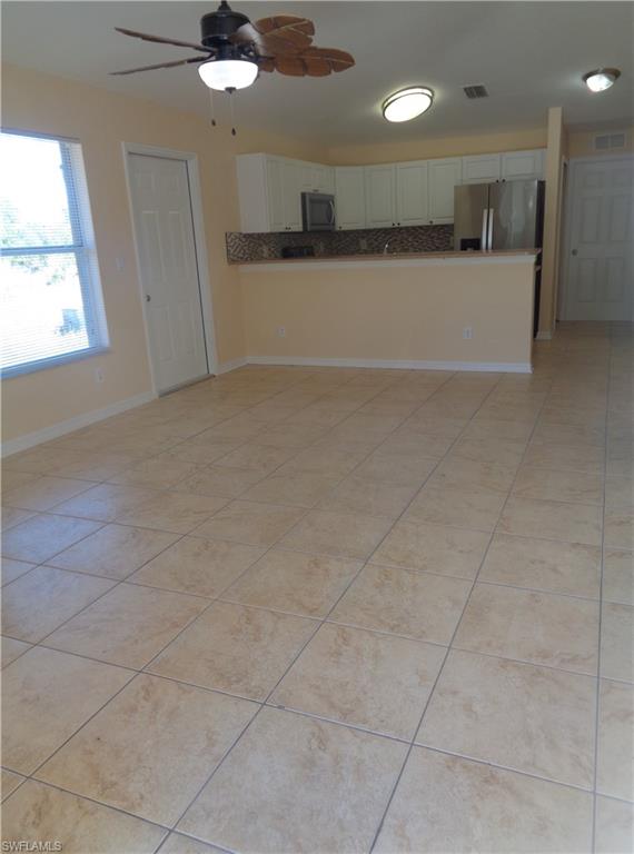 Family room and kitchen featuring white cabinets,  stainless steel appliances, ceiling fan and light tile patterned floors