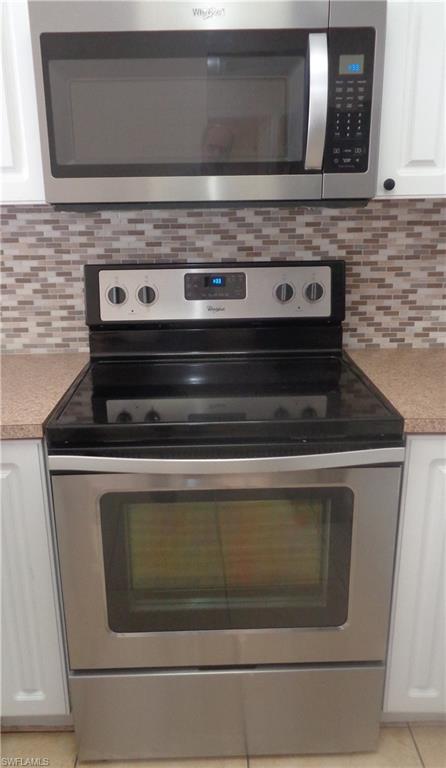 Kitchen with stainless steel microwave, stove & oven, backsplash, white cabinetry, and light countertops