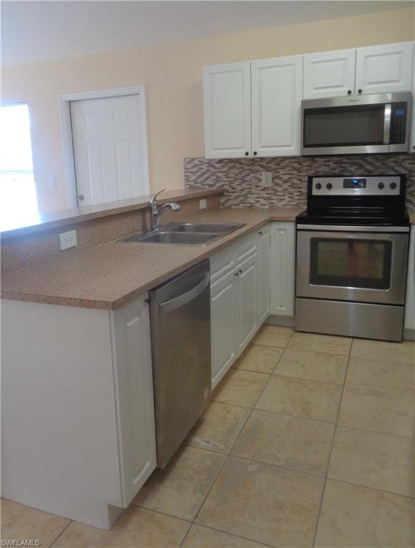 Kitchen featuring white cabinets, backsplash, stainless steel dishwasher, microwave, stove & oven, backsplash, light tile patterned floors, and light countertops